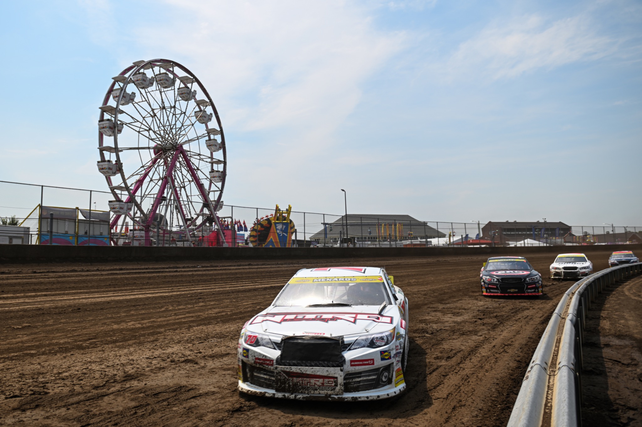 Dirt race car passing a Ferris wheel at an evening event