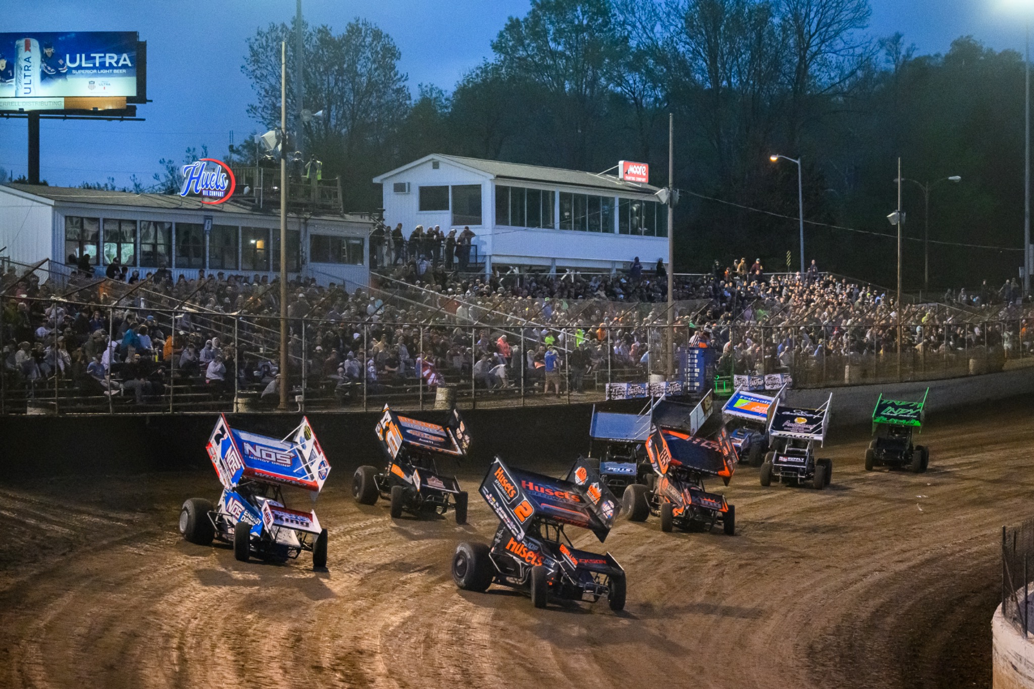 Sprint cars racing at an evening event with the crowd in view