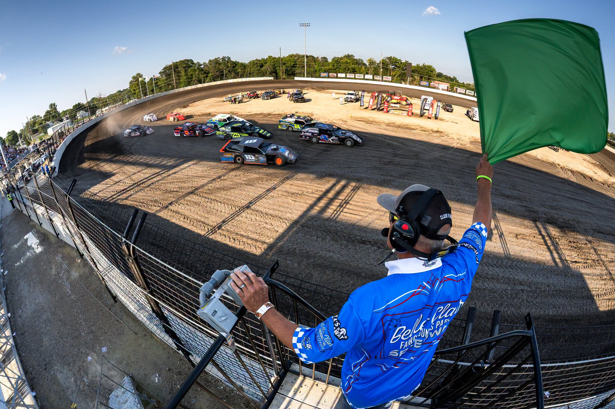 Flagman waving the green flag above a full dirt-track starting field