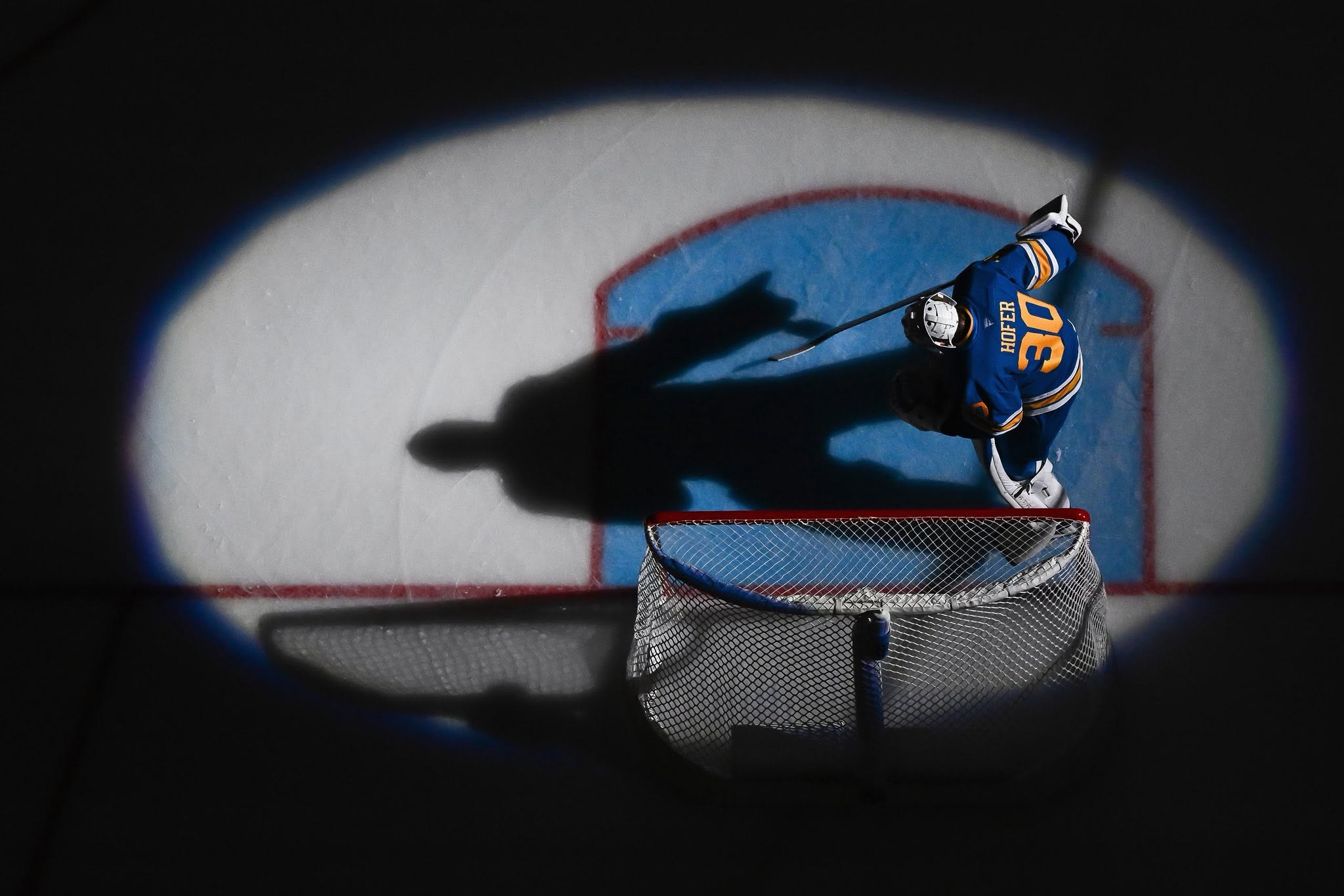 Overhead view of a hockey goaltender and dramatic shadow across the crease
