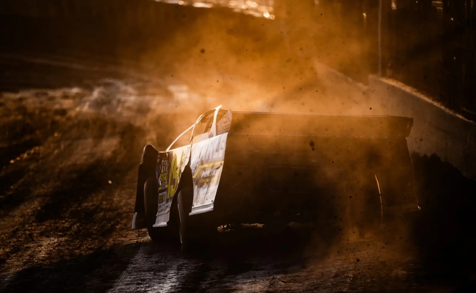 Dirt late model backlit by golden light and airborne dust on track
