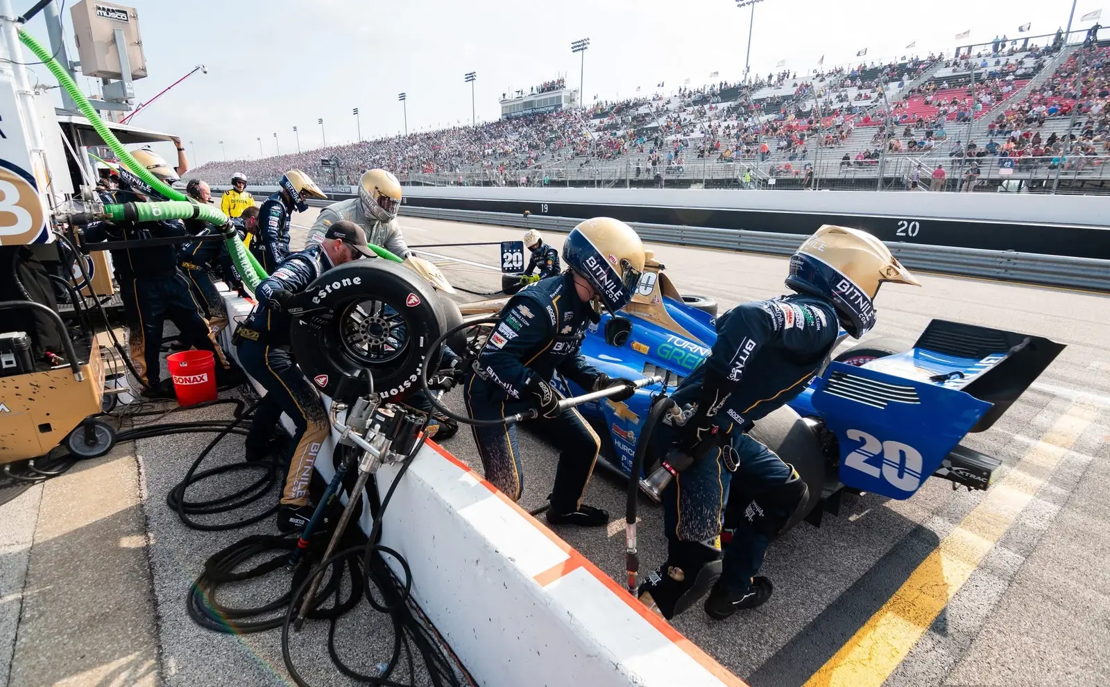 IndyCar pit crew servicing a blue number 20 car during a pit stop