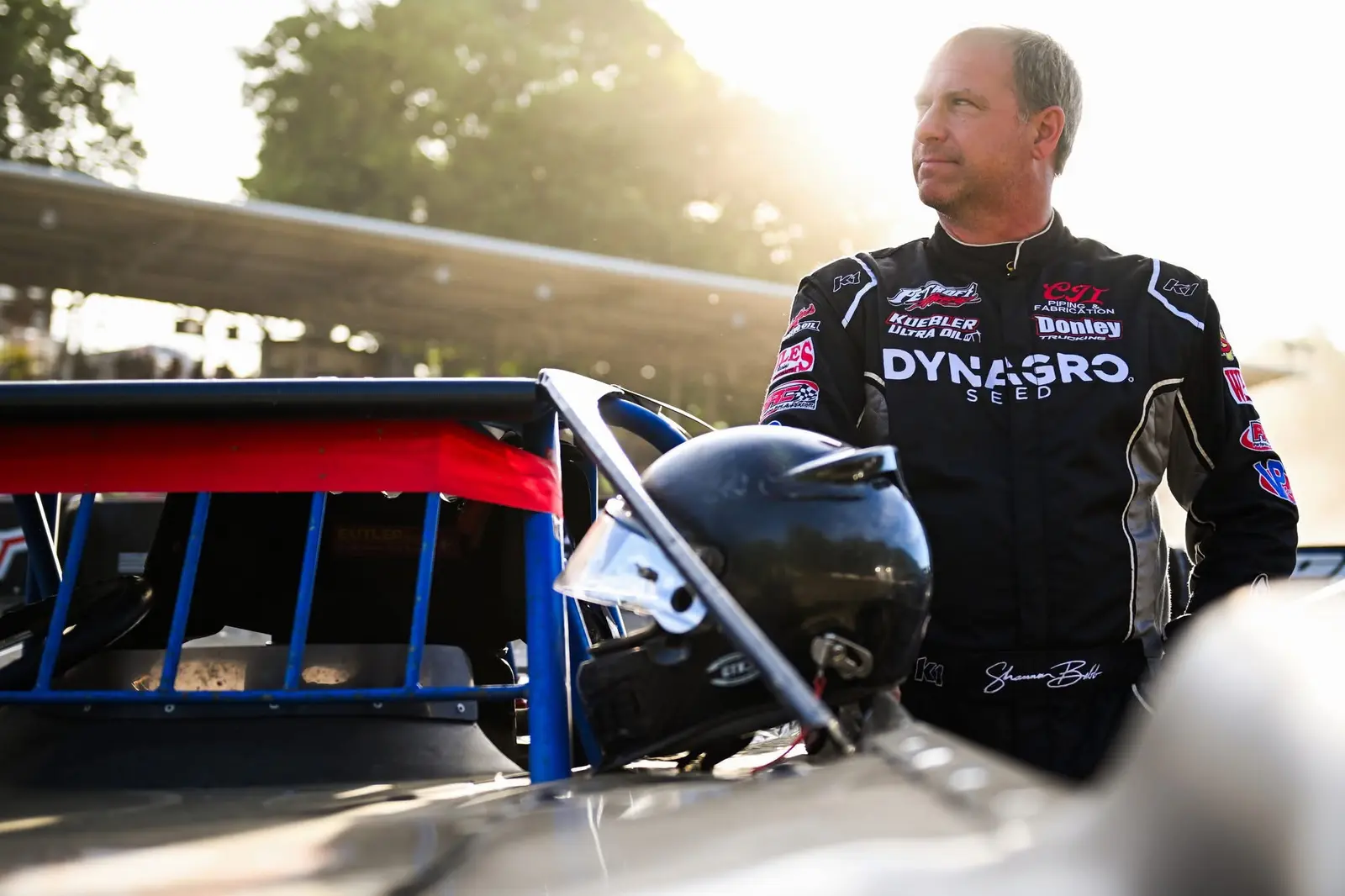 Dirt late model driver standing beside his car in golden-hour light