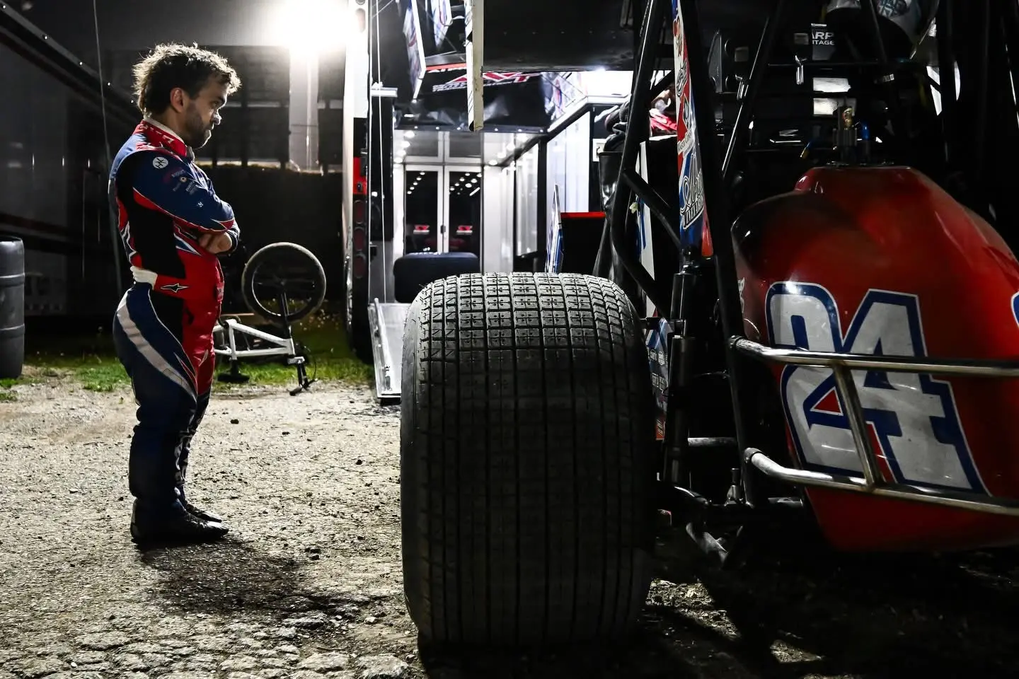 Sprint car driver standing beside his race car and rear tire at night