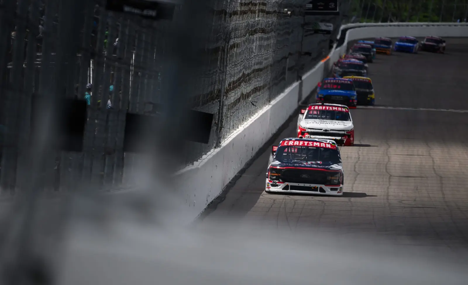 Pack of NASCAR trucks racing past the outside wall through tire smoke