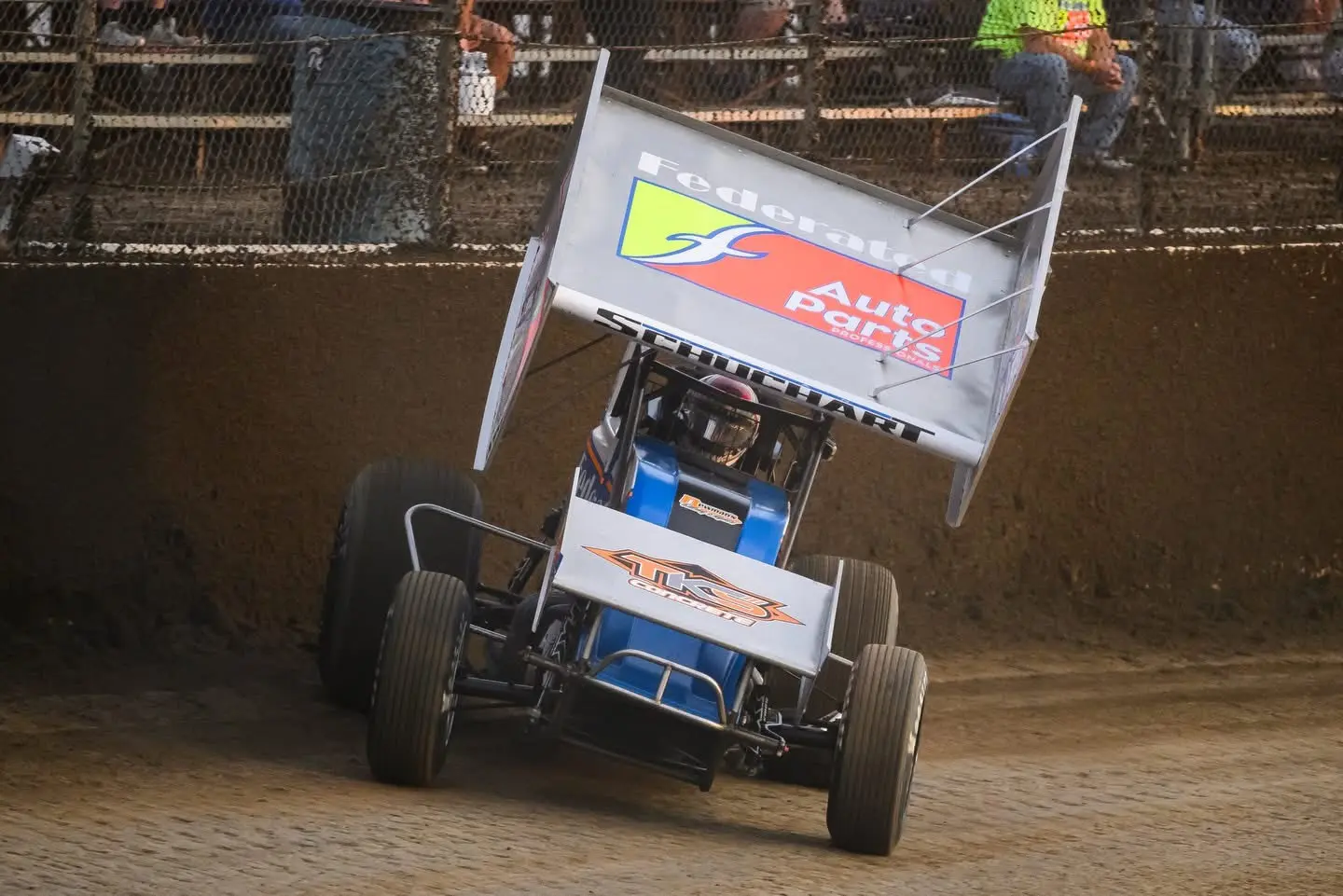 Winged sprint car racing through a dirt-track corner
