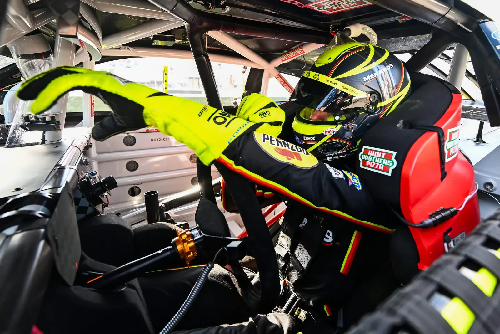 Helmeted race driver adjusting equipment while seated inside a race car cockpit