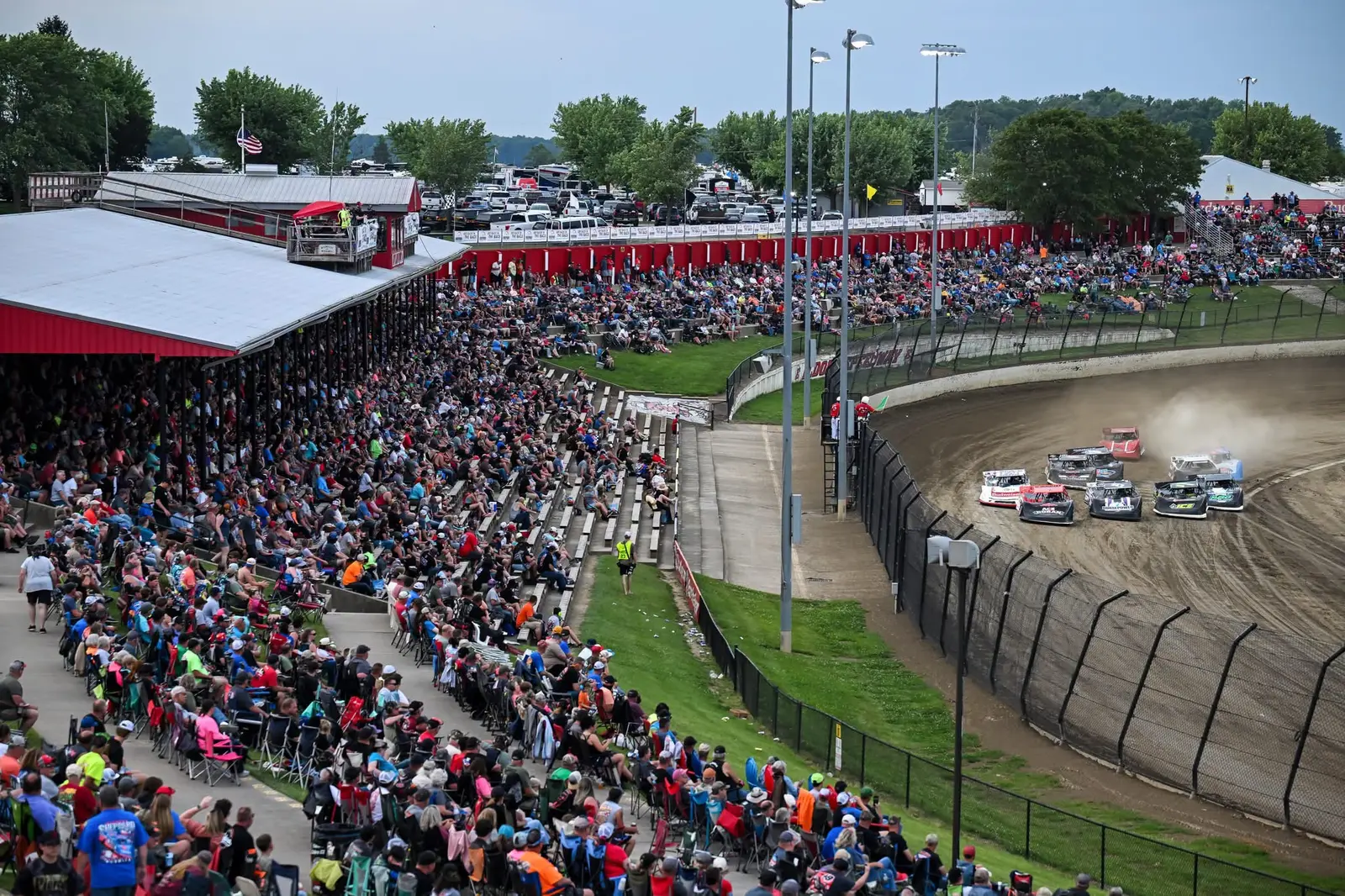 Packed grandstands surrounding a dirt-track race on a summer afternoon