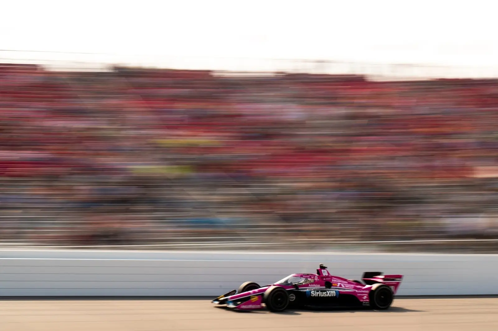 Pink IndyCar racing past packed grandstands in a controlled panning photograph