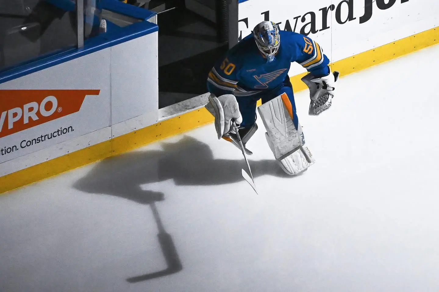 Hockey goaltender entering the ice beside a dramatic stick-shaped shadow