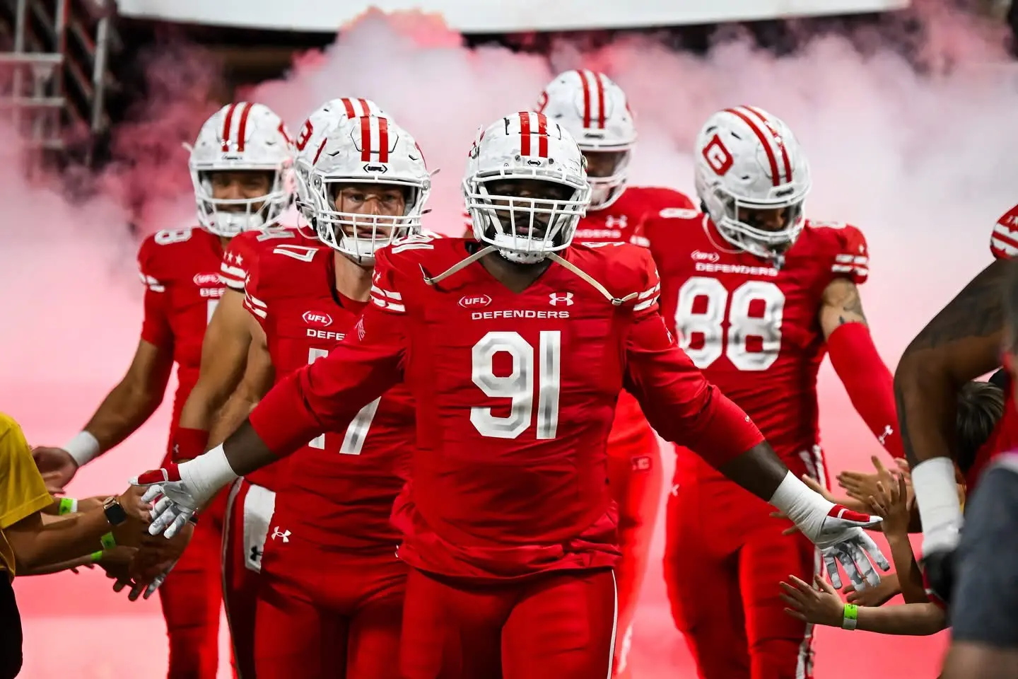Professional football players entering the field through red smoke and reaching fans