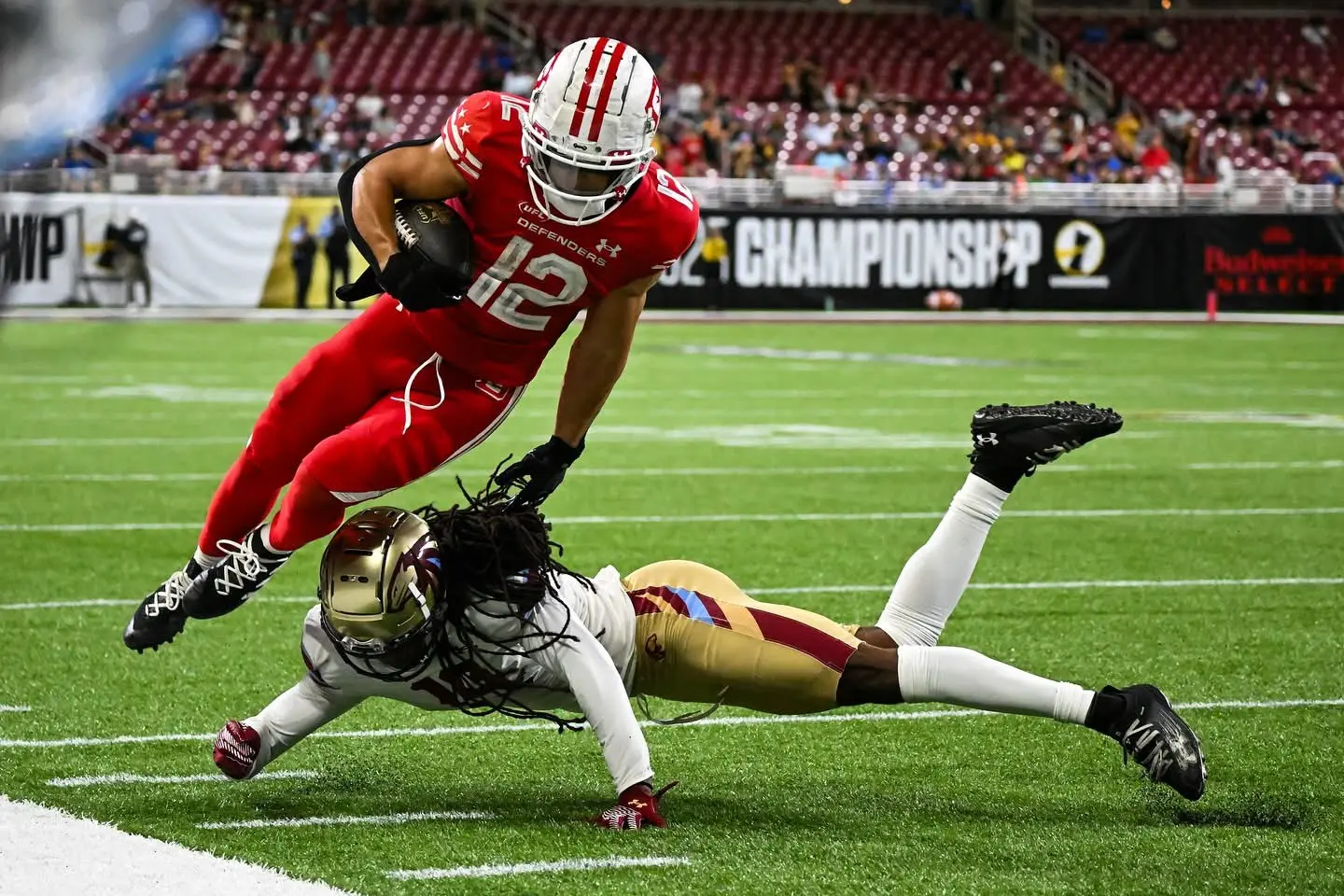 Professional football player hurdling a diving defender near the sideline
