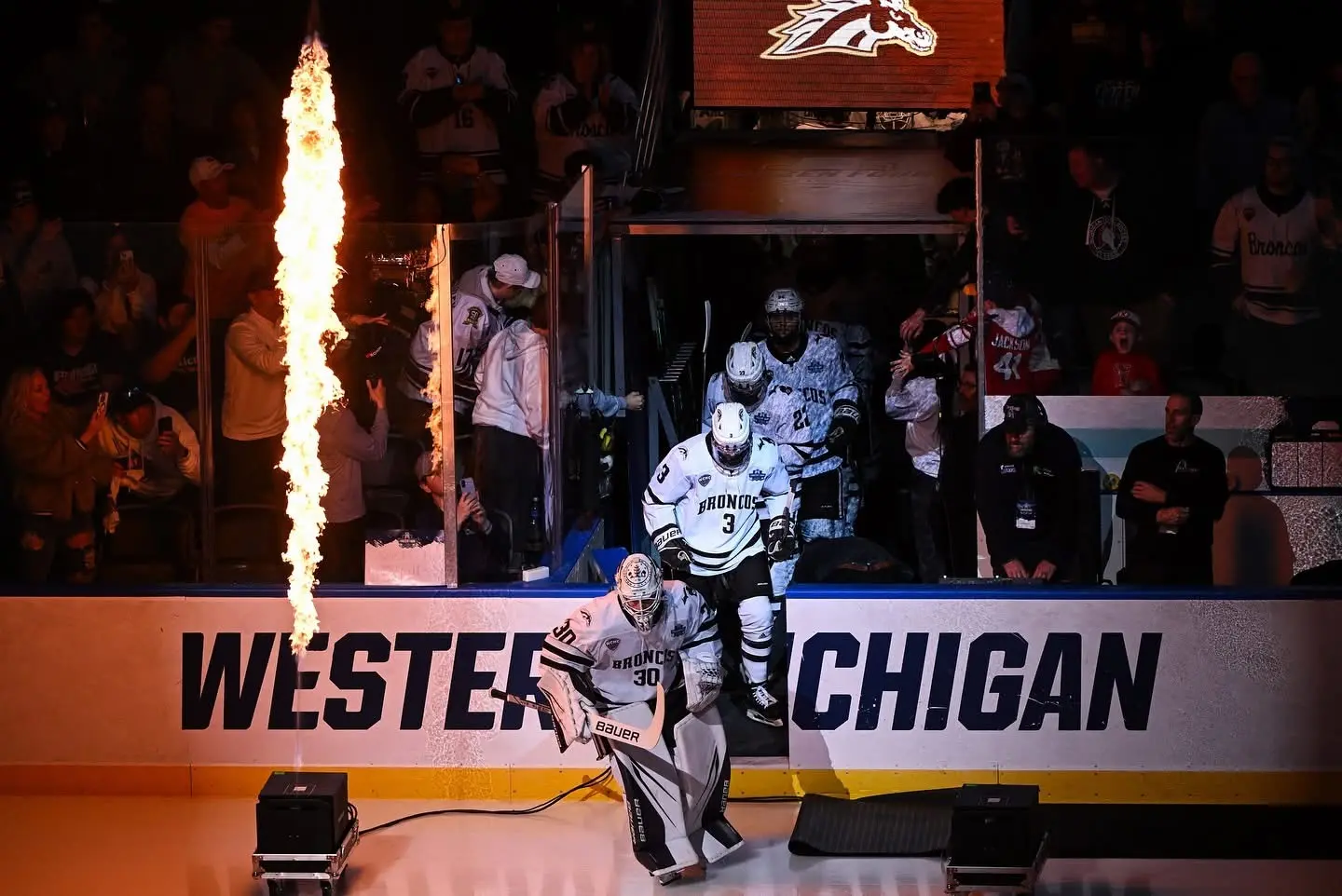 Hockey goaltender leading teammates onto the ice beside a column of flame