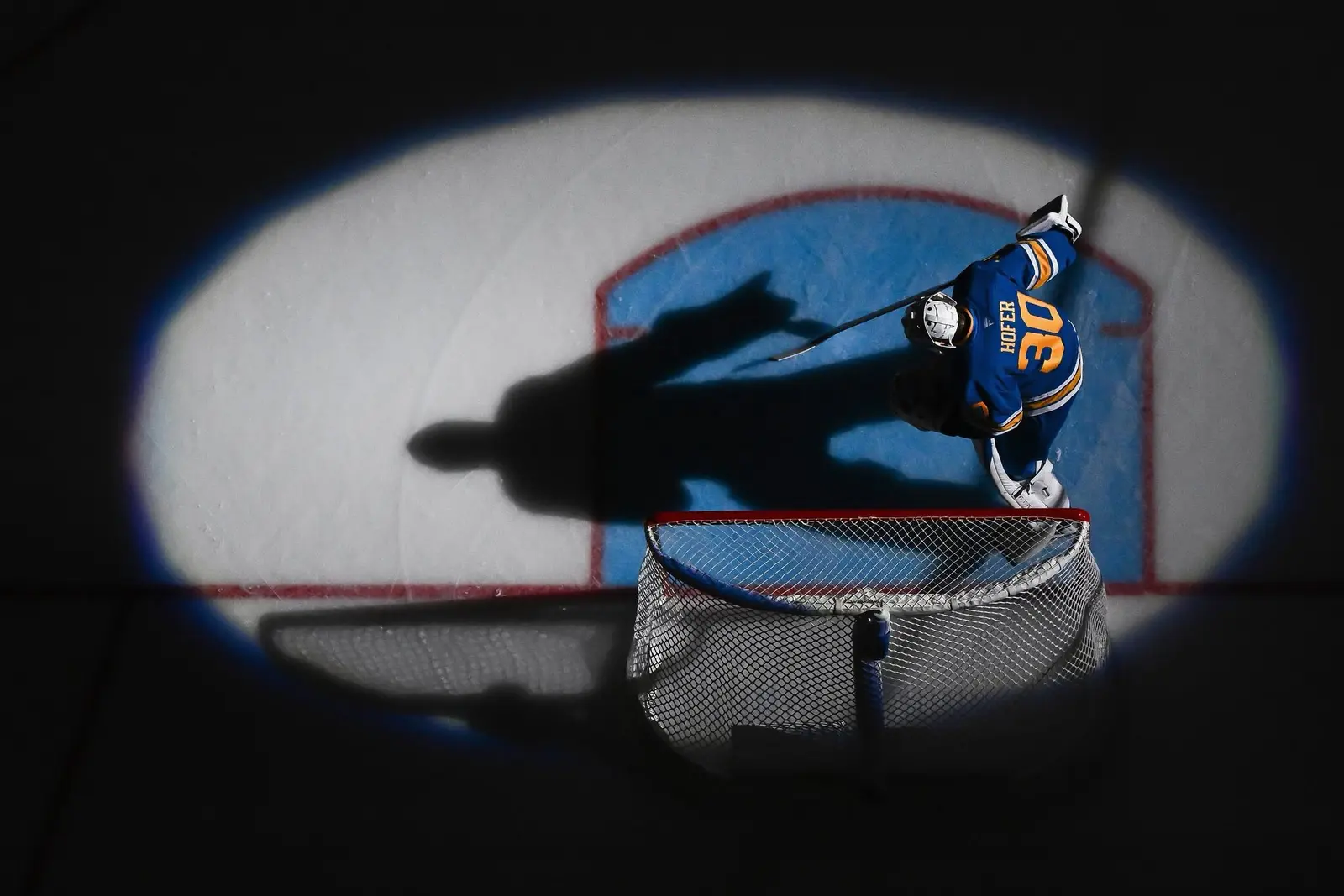 Overhead view of a hockey goaltender and dramatic shadow across the crease
